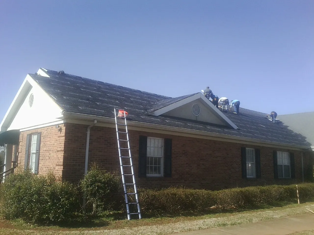 Crew tearing shingles off a brick ranch roof with a ladder set — Emergency Roof Repair work by our crew in Boalsburg