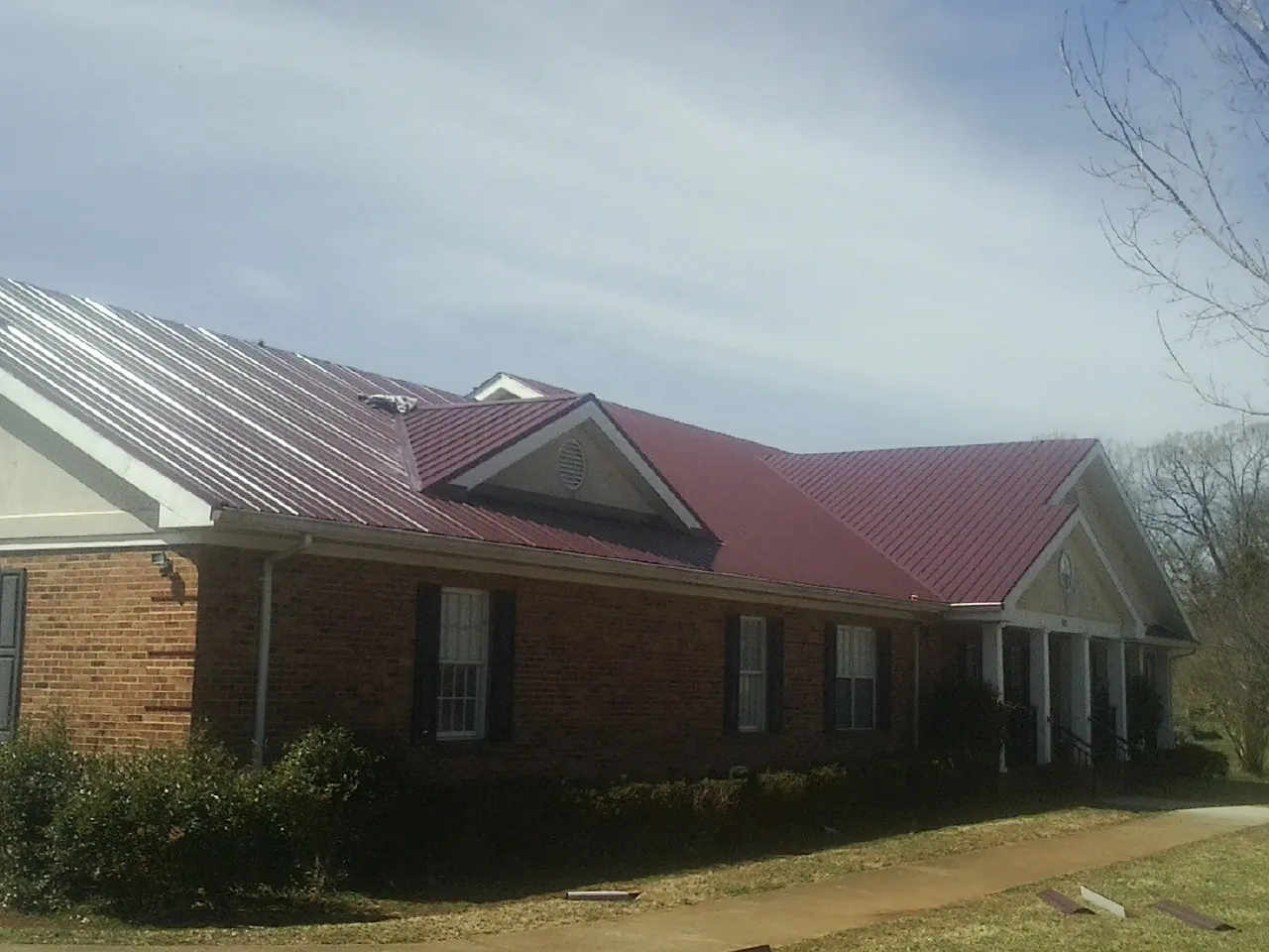 Red metal roof with gabled entries on a long brick building, from a Hail Damage Roof Repair job in Boalsburg