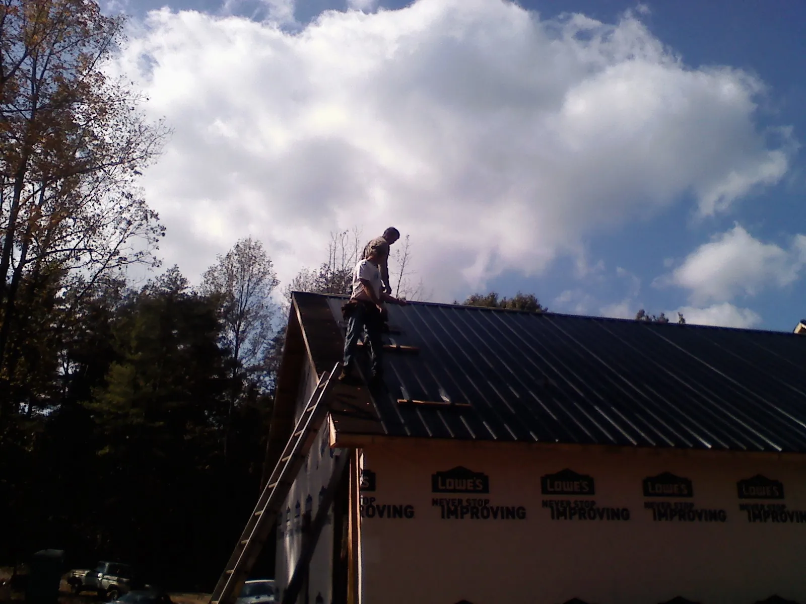 Roofer fastening dark metal panels high against a cloudy sky, from a Roof Inspection job in Boalsburg
