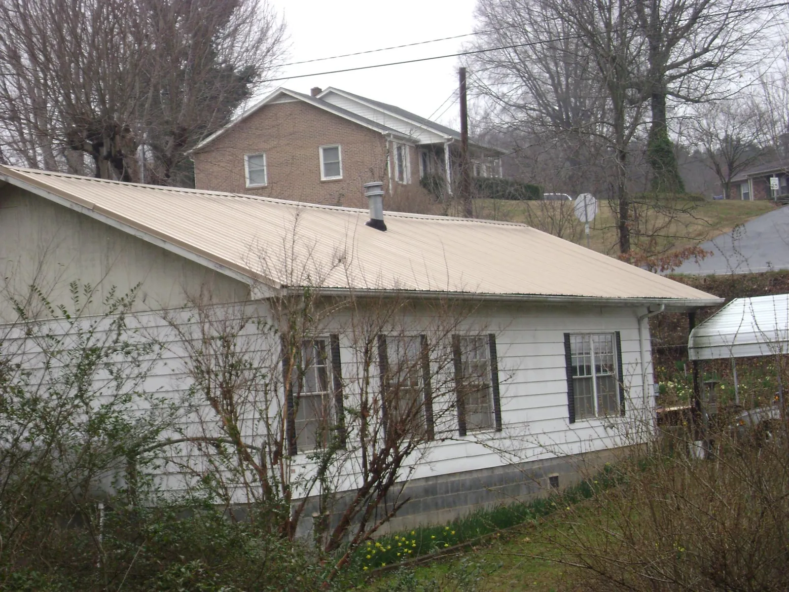 Tan metal roof on a white sided house set into a hillside — Commercial Roofing by Roofing Brothers in Boalsburg